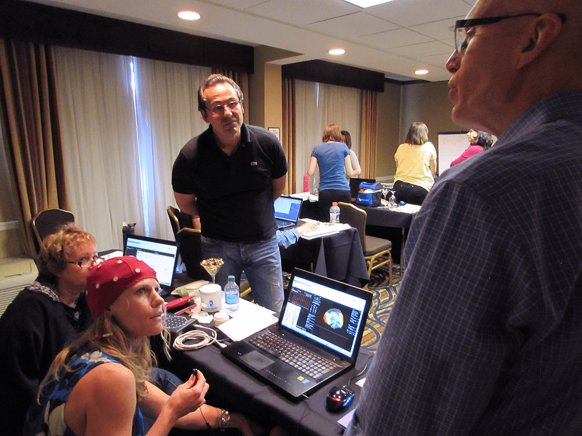 An instructor answering a question at a StressTherapy Solutions workshop, beside an attendee wearing an EEG cap