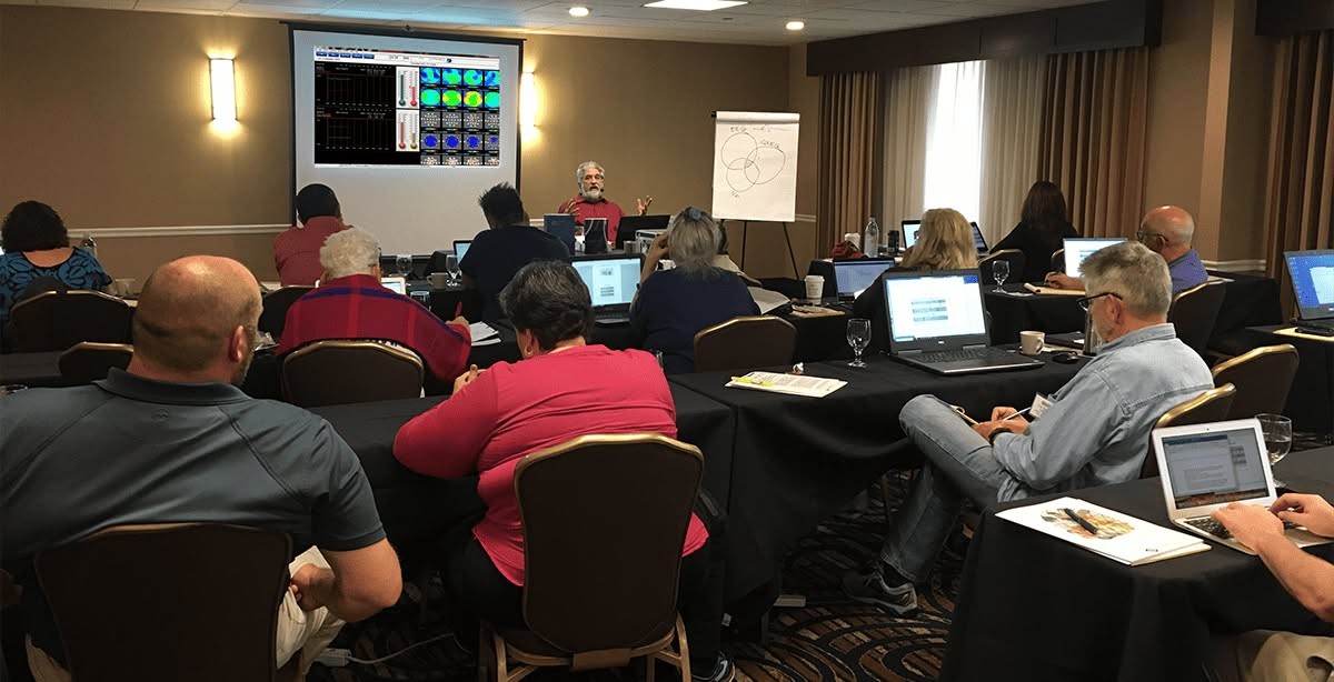 A StressTherapy Solutions neurofeedback workshop in session, with attendees at laptops and an EEG display on screen